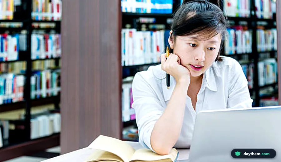 Nữ sinh châu Á đang tập trung sử dụng laptop và mở sách học tập tại một thư viện hiện đại