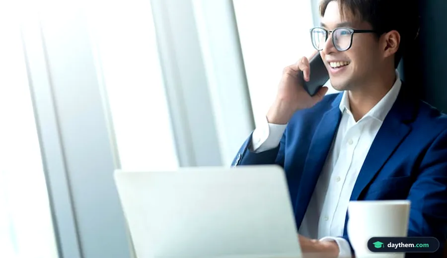 Nam nhân viên mặc trang phục lịch sự, đeo kính thông minh và cầm điện thoại khi đang làm việc với laptop tại bàn làm việc không gian chung.