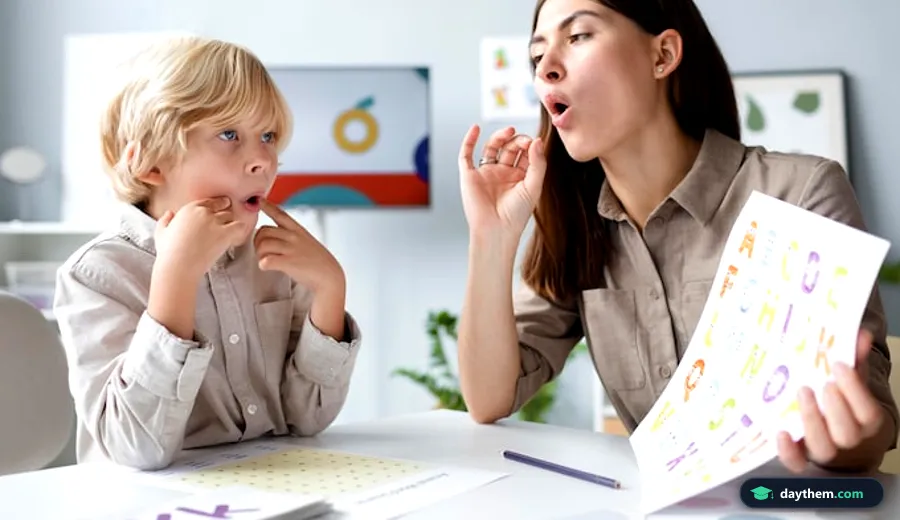 Cô giáo hoặc phụ huynh đang ngồi cạnh, chỉ dẫn bé trai 4 tuổi học bài qua sách hoặc thẻ hình